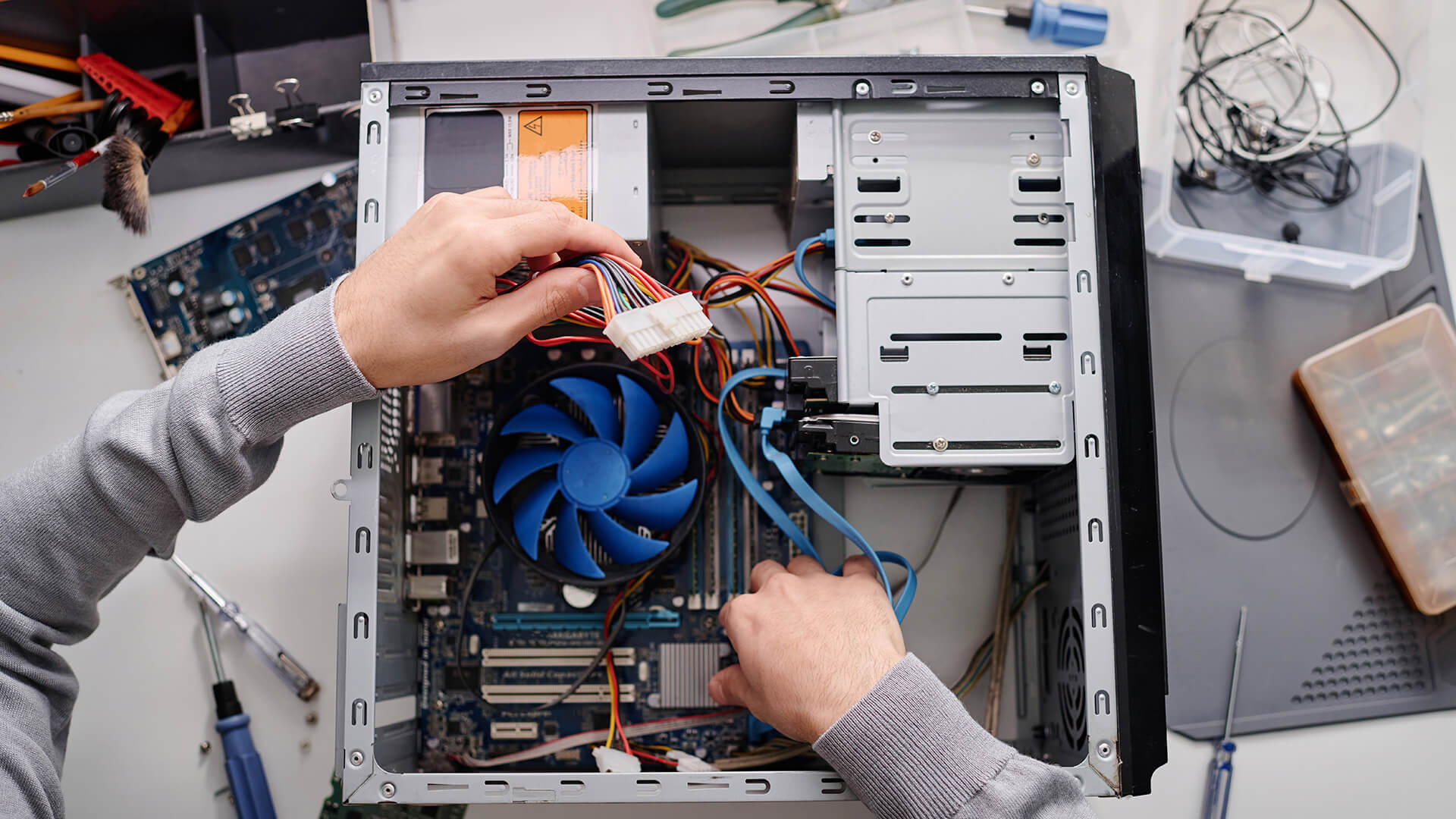 Conserto de computador aberto com t&eacute;cnico verificando componentes internos, incluindo placa-m&atilde;e, cooler e cabos de energia, em ambiente de oficina.