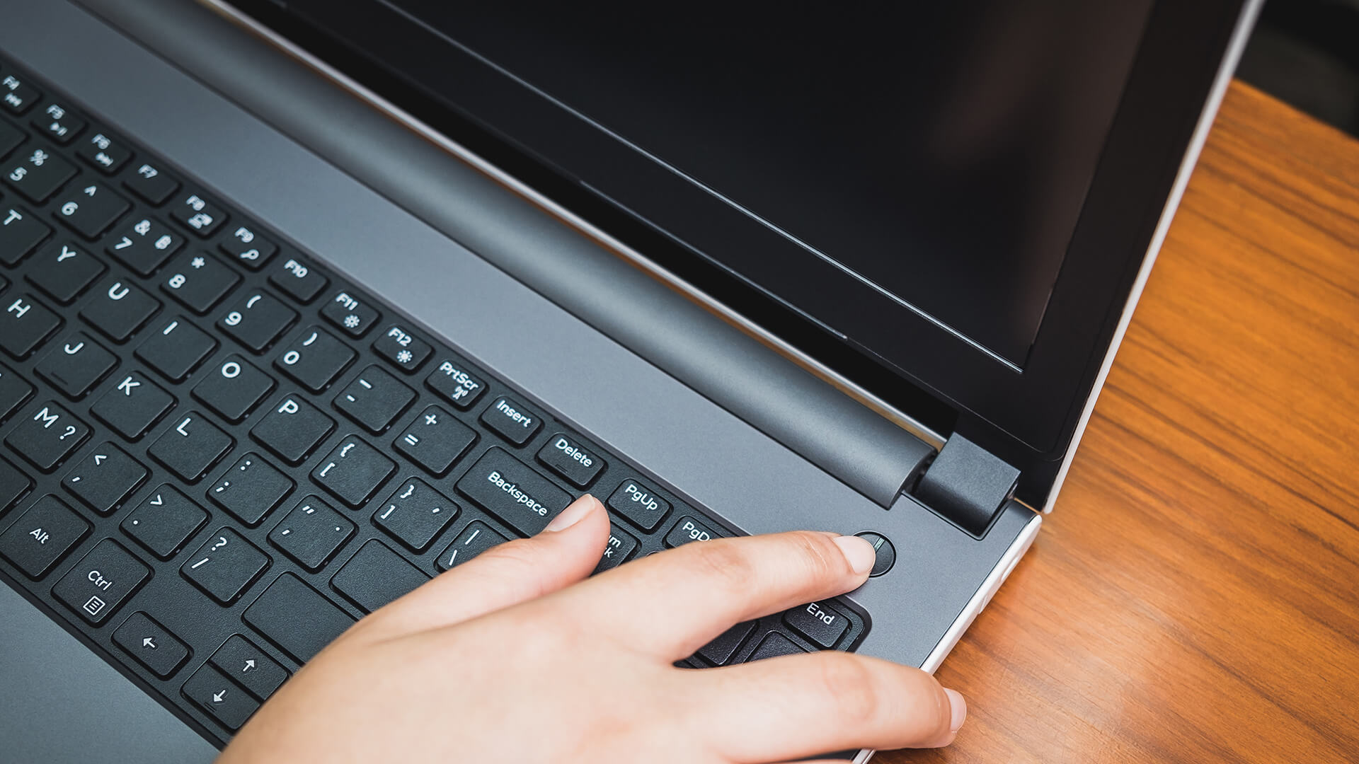 Pessoa usando laptop para trabalhar ou estudar, teclado de computador port&aacute;til com foco na m&atilde;o e teclado, superf&iacute;cie de madeira ao fundo.