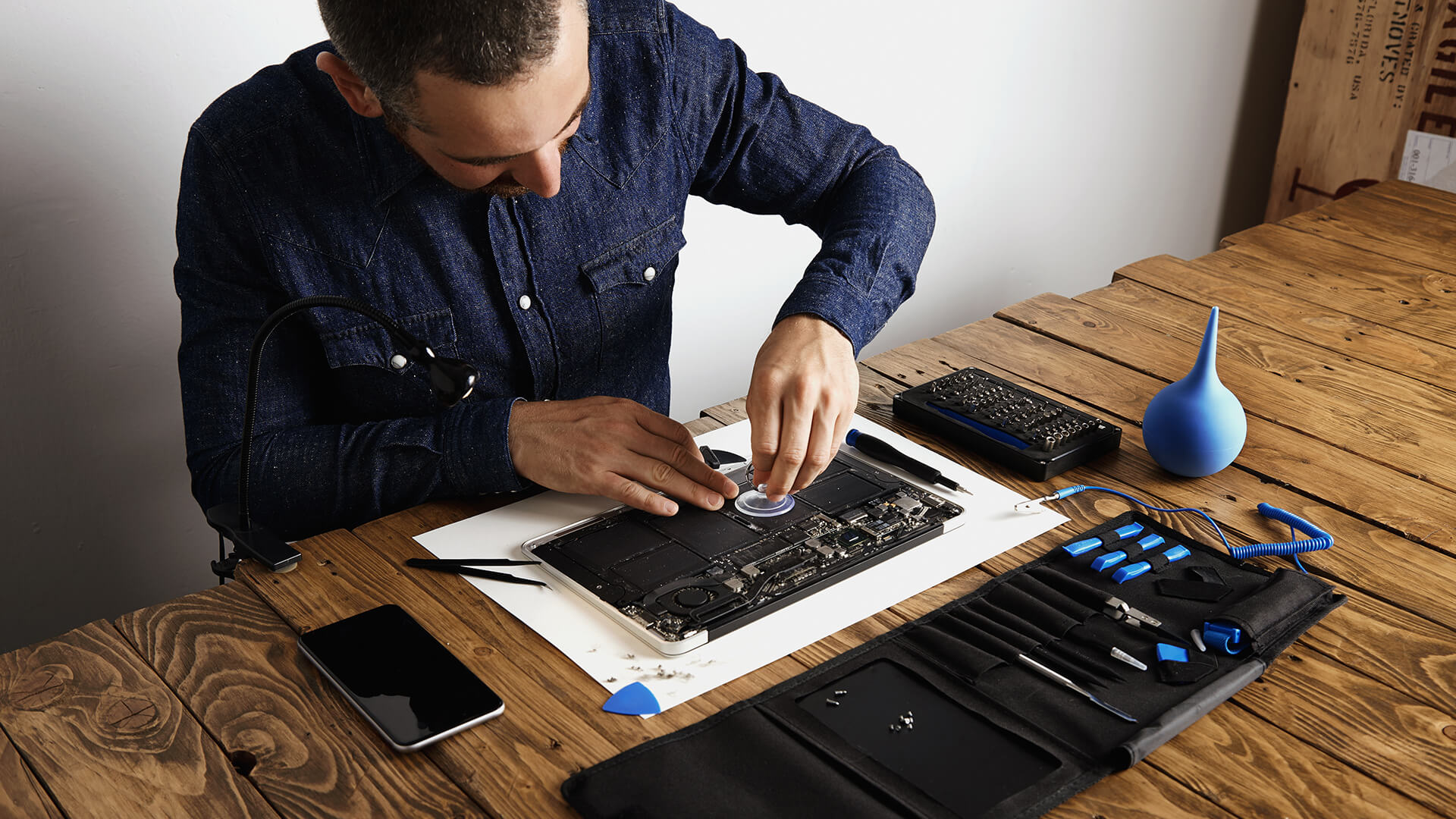 Técnico realizando reparo em placa-mãe de um laptop com ferramentas especializadas em um ambiente de trabalho organizado e bem iluminado.